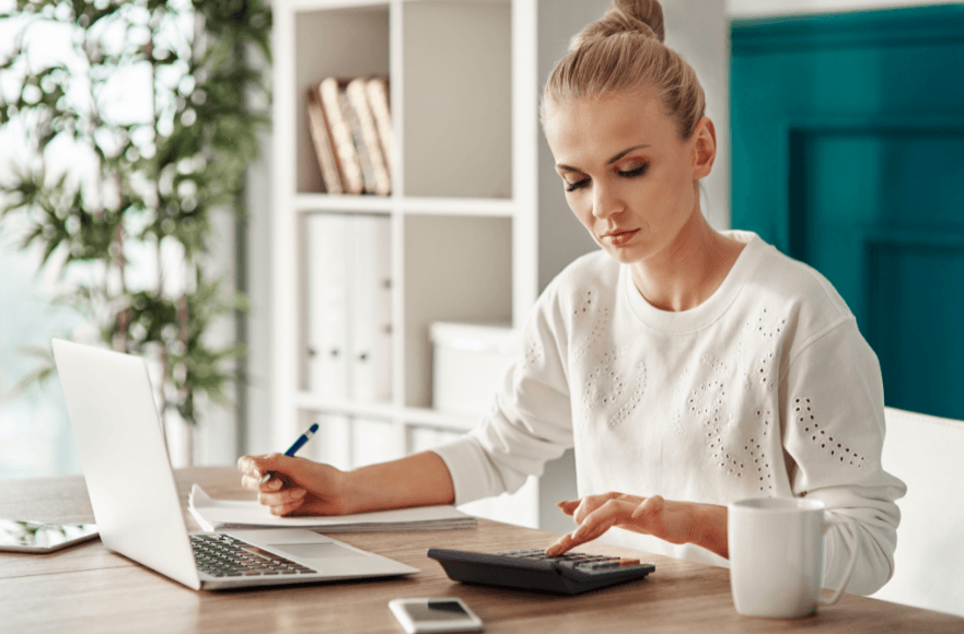 Frau sitzt am Laptop und bedient Taschenrechner nebenbei